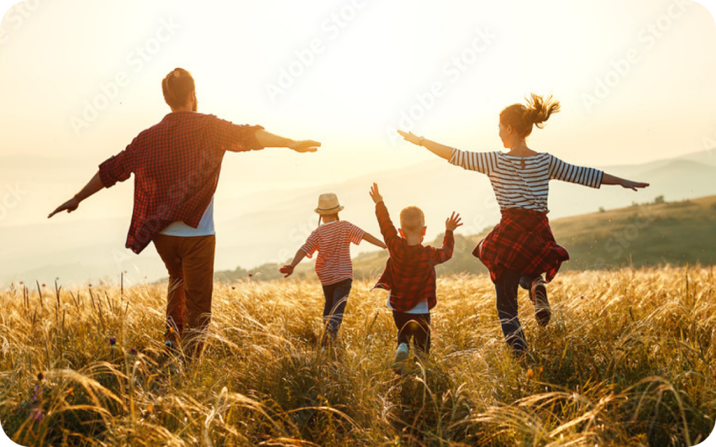 Parents with two young children running through a field at sunset